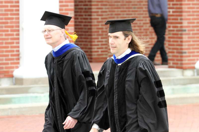 a man in black graduation gowns and cap and gowns walking