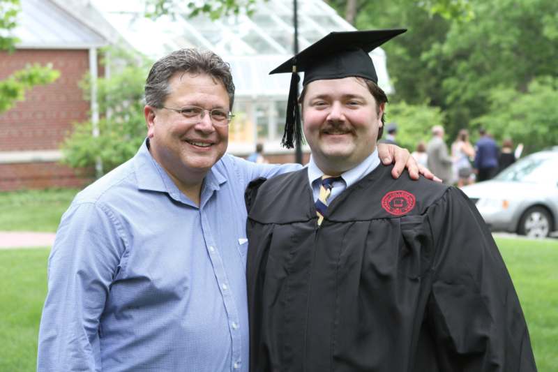 a man in a graduation gown and cap standing next to a man