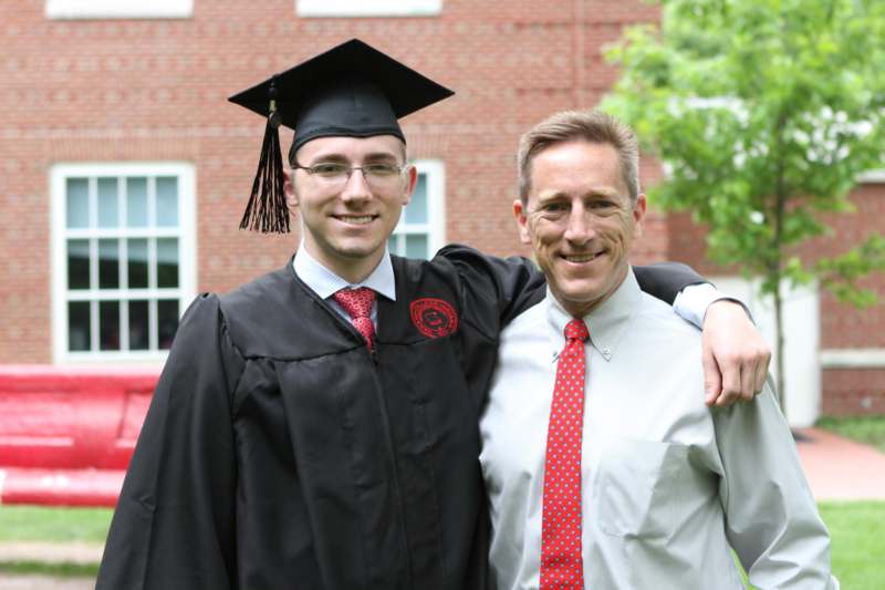 a man in a graduation gown and cap with his arm around another man