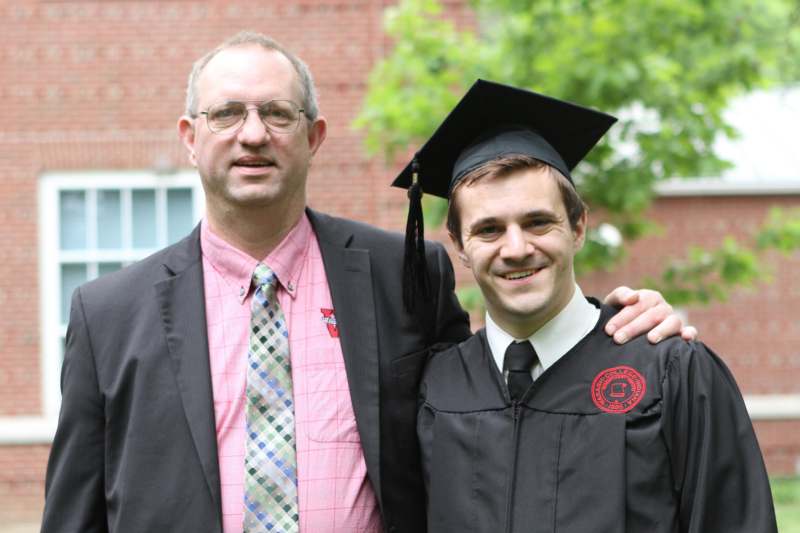 a man in a suit and cap standing next to a man in a graduation gown