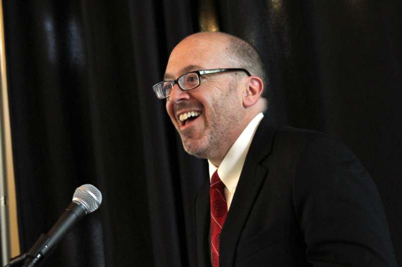 a man in a suit and tie laughing at a microphone