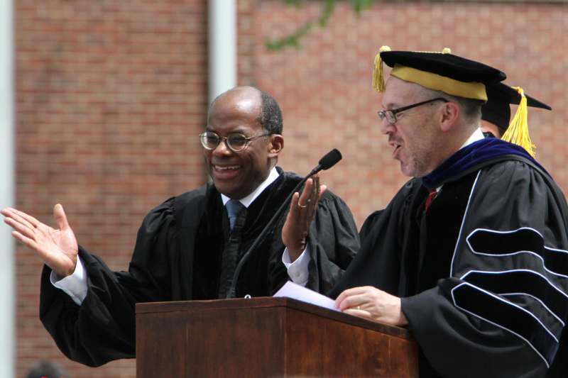 a man in black gowns and glasses standing at a podium