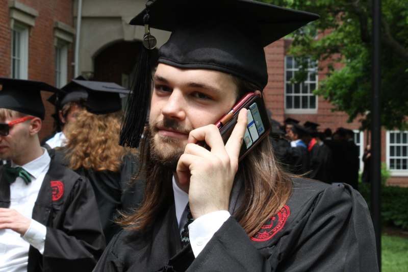 a man in a graduation gown talking on a cell phone
