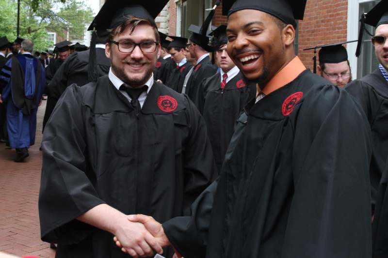 a group of men in graduation gowns shaking hands
