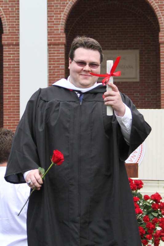 a man wearing a graduation gown holding a rose