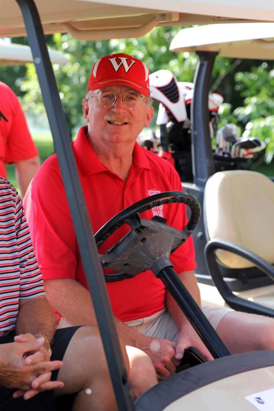 a man in a red shirt and hat driving a golf cart