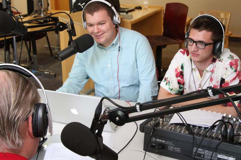 two men sitting at a desk with a laptop and a microphone