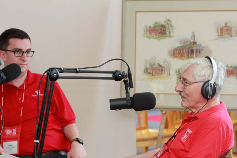 a man in red shirt talking to another man in a microphone