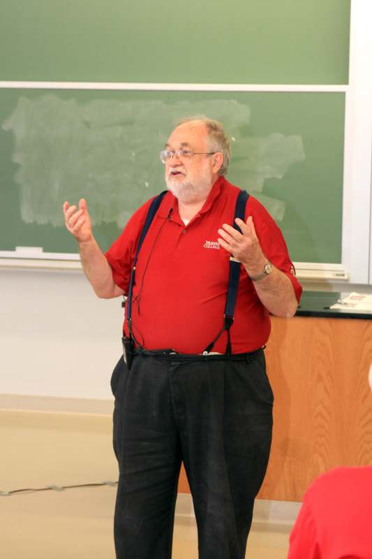 a man in a red shirt and suspenders standing in front of a chalkboard