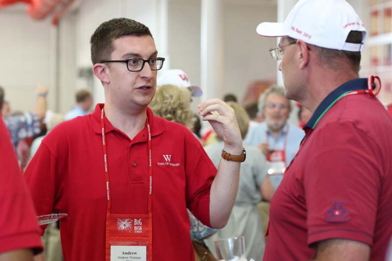 a man wearing a red shirt and glasses talking to another man