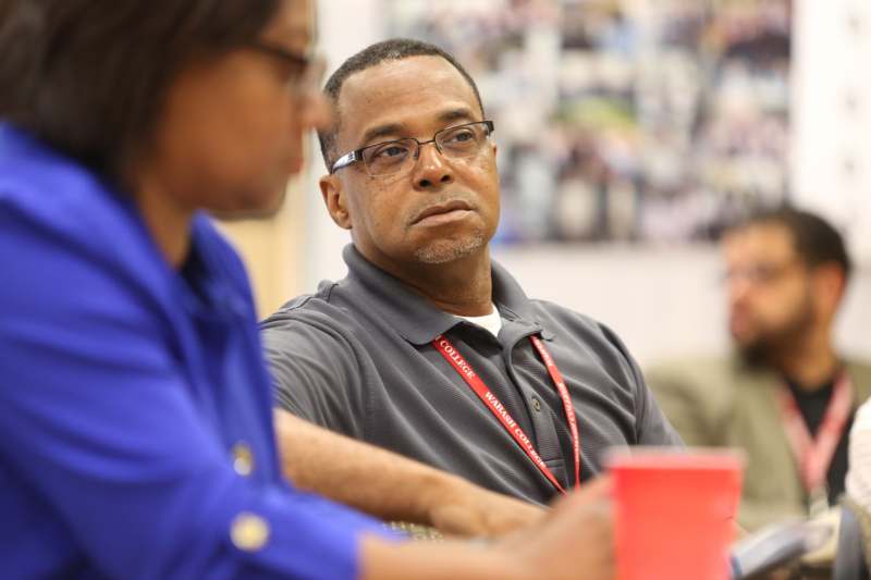 a man wearing glasses and a lanyard sitting at a table