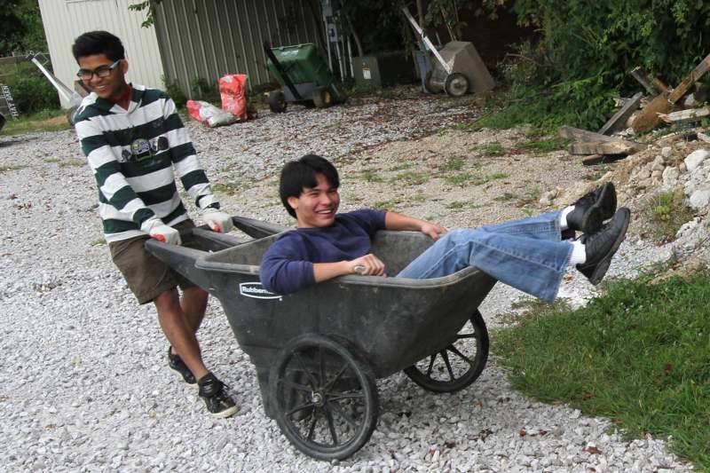 a man pushing a wheelbarrow with another man in it