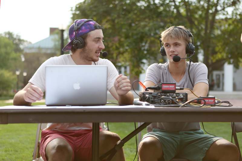 two men sitting at a table with a laptop and a radio