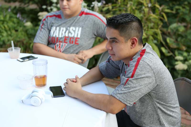 a man sitting at a table with a cell phone and a man in the background