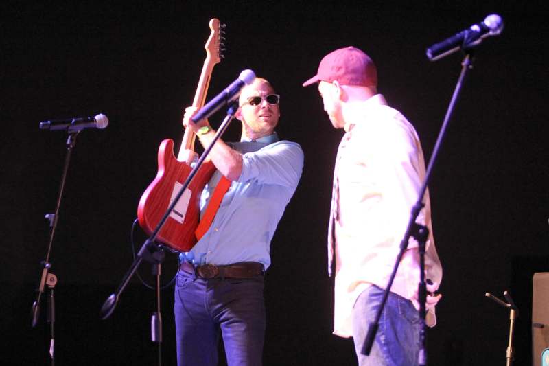 a man holding a guitar and another man standing on a stage