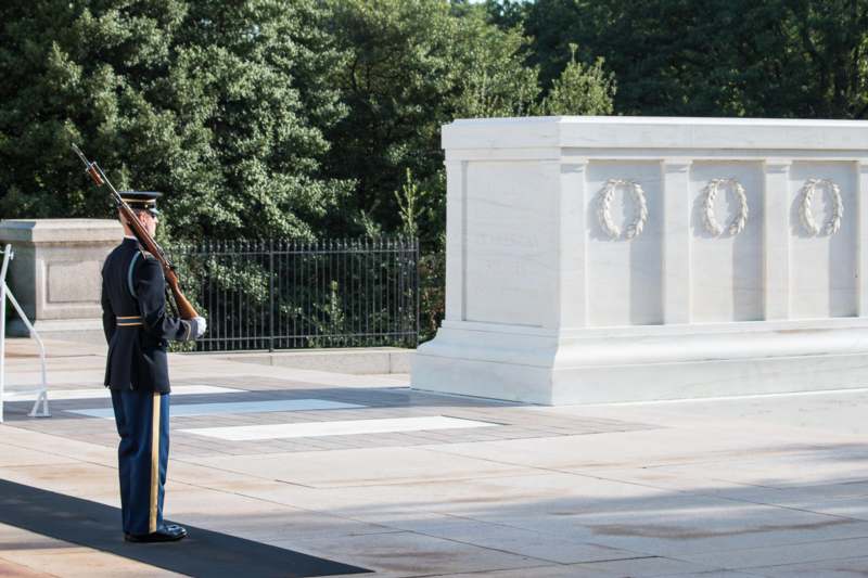 a soldier in uniform standing in front of a white monument with Tomb of the Unknowns in the background