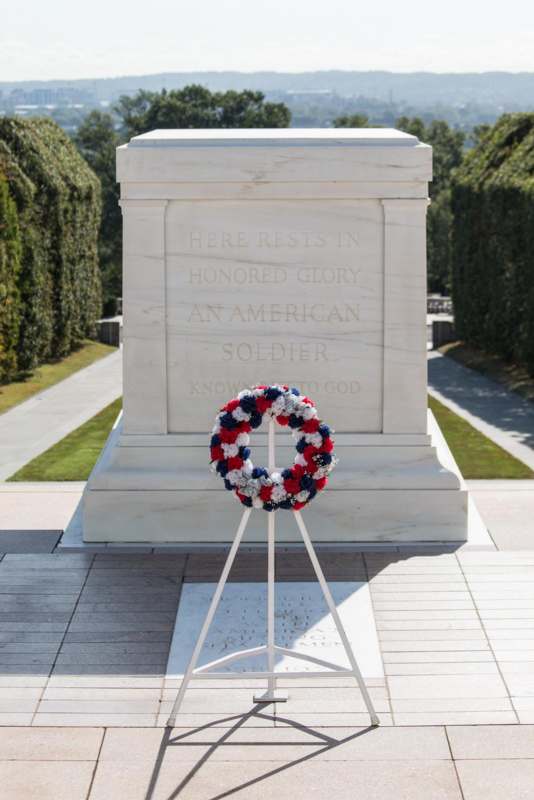 a wreath on a stand in front of a monument with Tomb of the Unknowns in the background