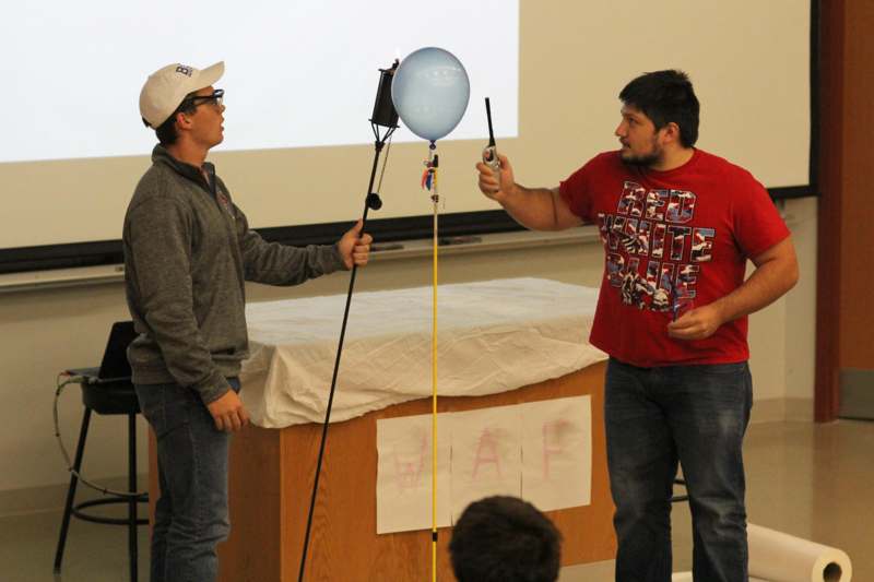 a man holding a balloon and standing next to a man holding a stick