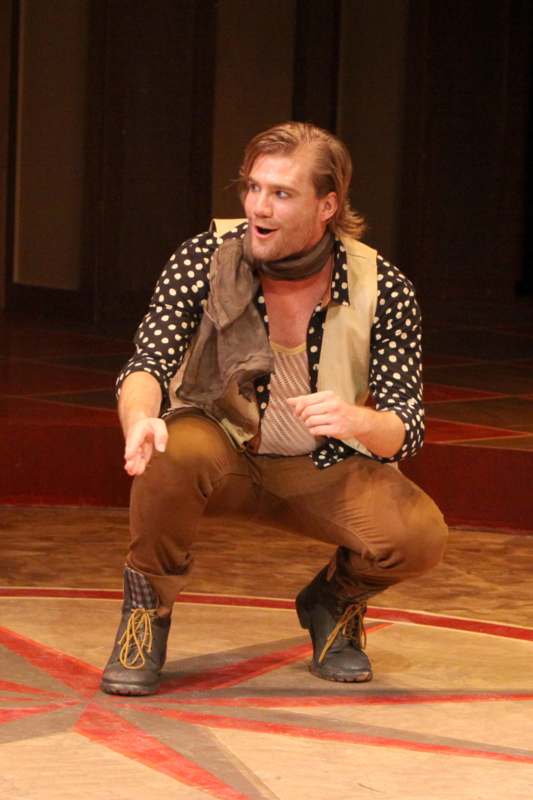 a man in a polka dot shirt and brown pants squatting on a stage