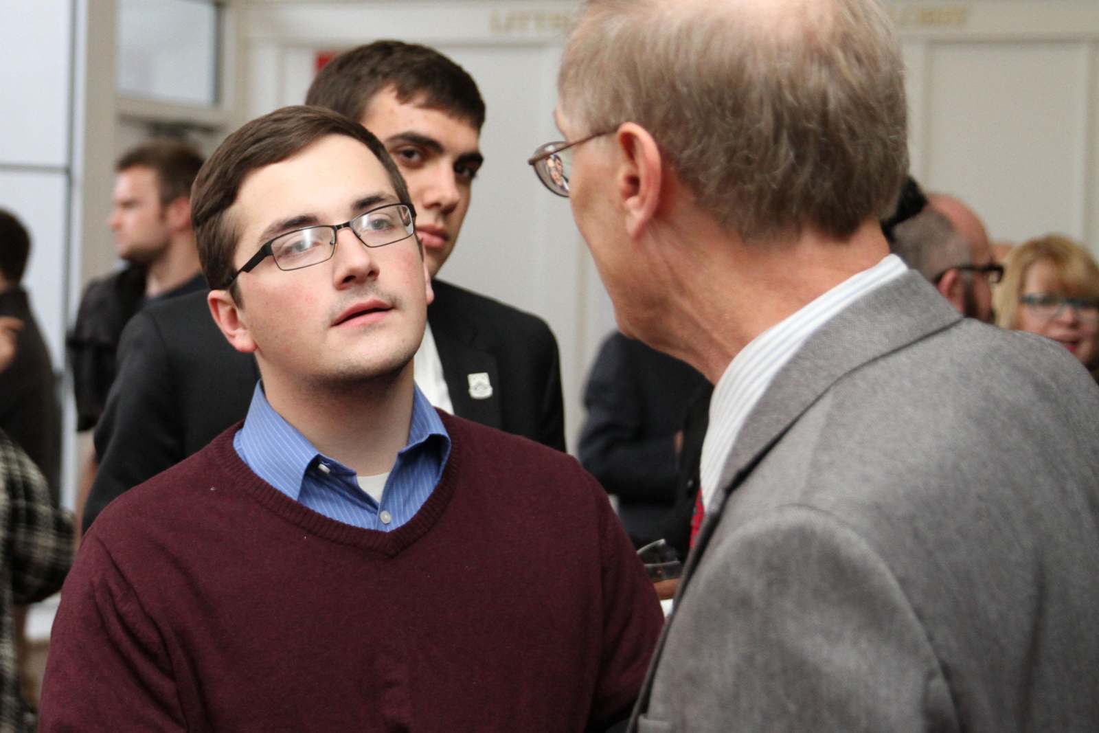 a man in a red sweater talking to a man in a suit
