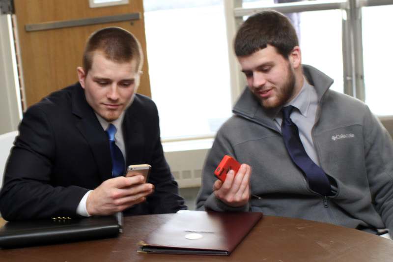two men sitting at a table looking at their phones
