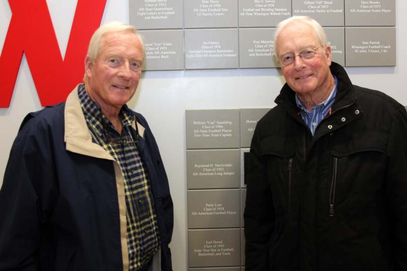two men standing next to a wall with silver plaques