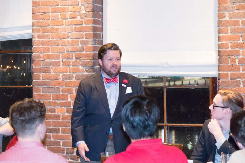 a man in a suit and bow tie standing in front of a group of people