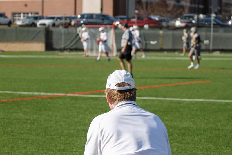a man sitting on a field with people playing lacrosse