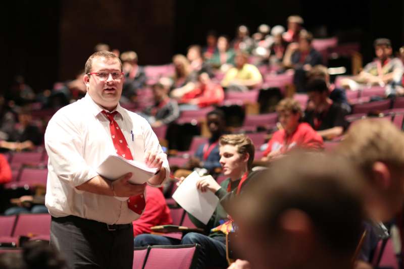 a man in a red tie holding a paper in front of a group of people