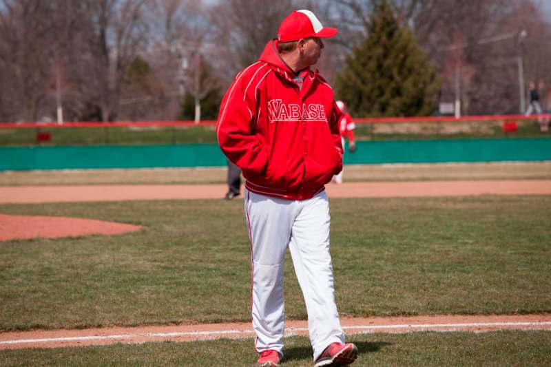 a man in a red jacket and white pants standing on a baseball field