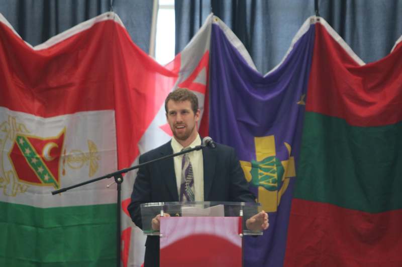 a man standing at a podium with flags behind him