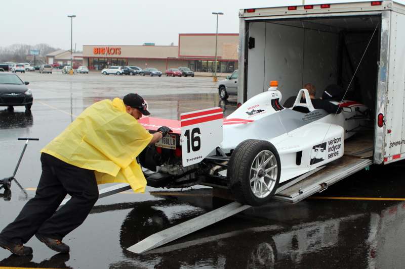 a man in a yellow raincoat pushing a race car