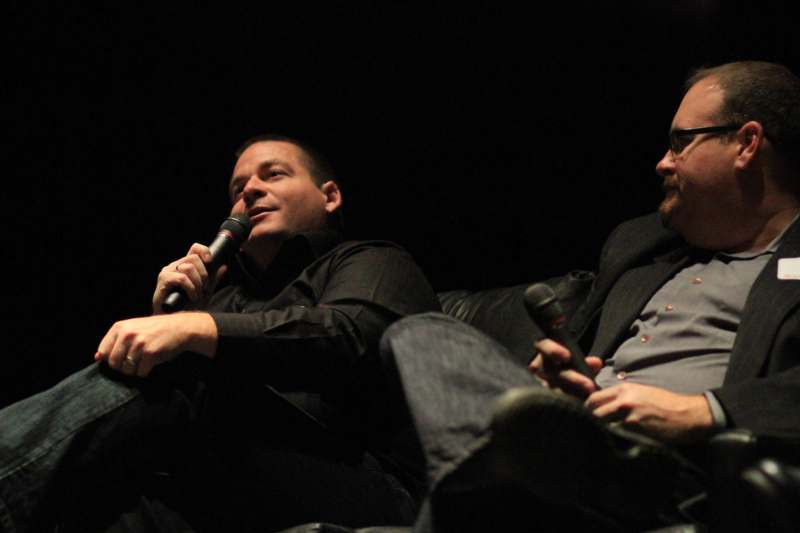 a pair of men sitting on a couch holding microphones