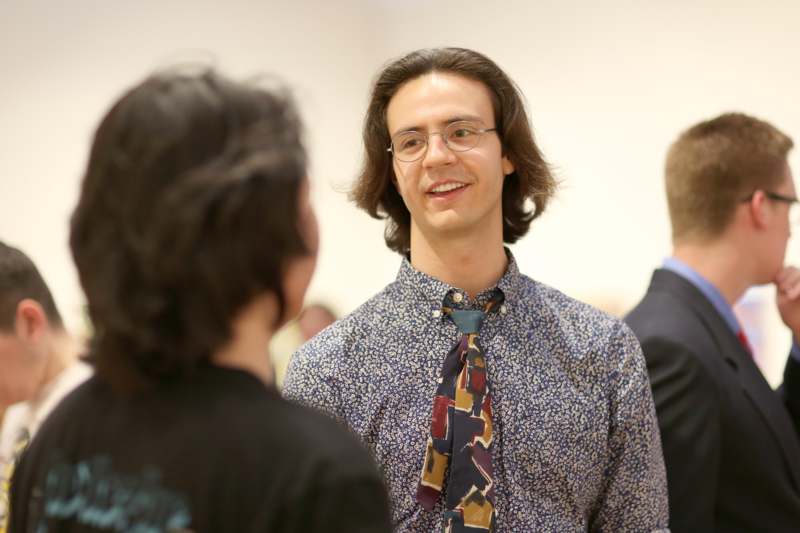 a man wearing glasses and a floral shirt talking to another man