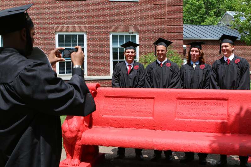 a group of people in graduation gowns and caps standing in front of a red bench