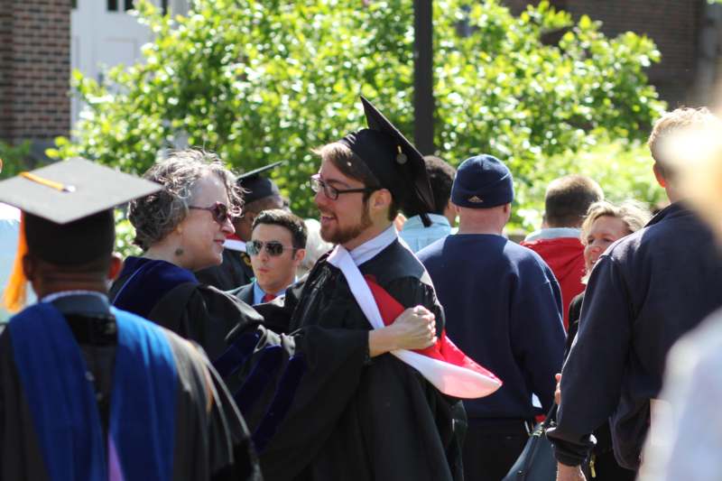 a man in a cap and gown hugging a woman in a crowd