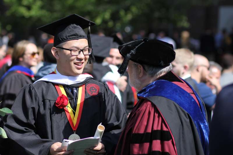 a man in graduation gowns and cap talking to another man
