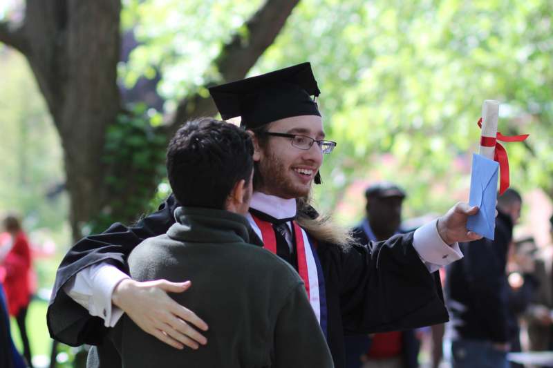 a man in a graduation gown and cap pointing to another man