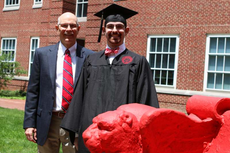 a man in a graduation gown and cap standing next to a red lion statue
