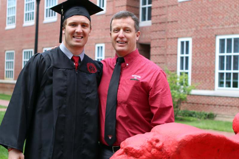 a man in a graduation cap and gown standing next to a man in a black gown