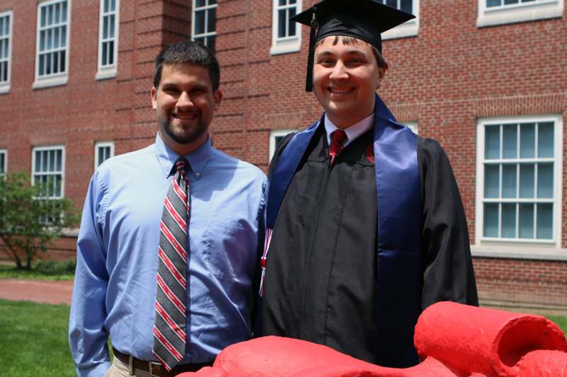 a man in a graduation cap and gown standing next to a man in a blue shirt
