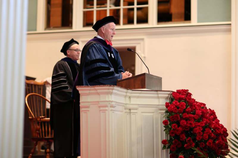 a man in graduation gowns and cap standing at a podium