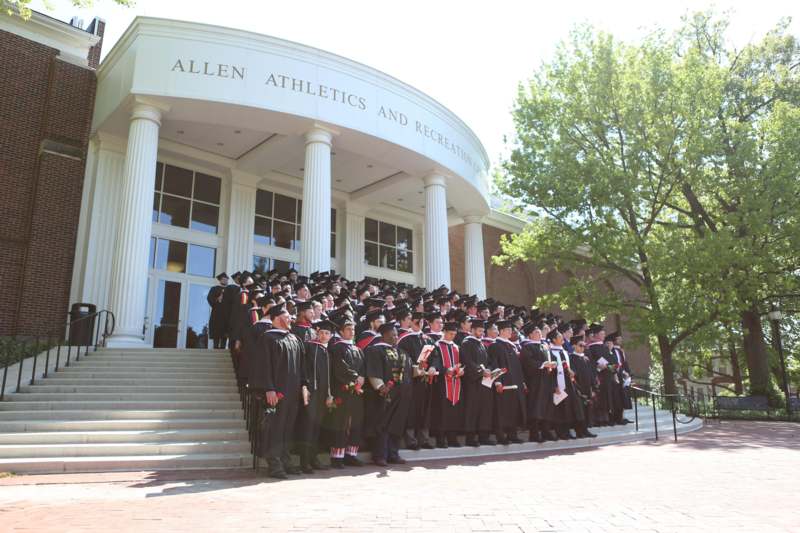 a group of graduates in black gowns and caps standing in front of a building