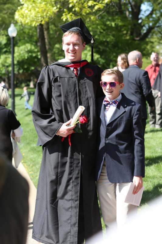 a man in a graduation gown and cap standing next to a boy