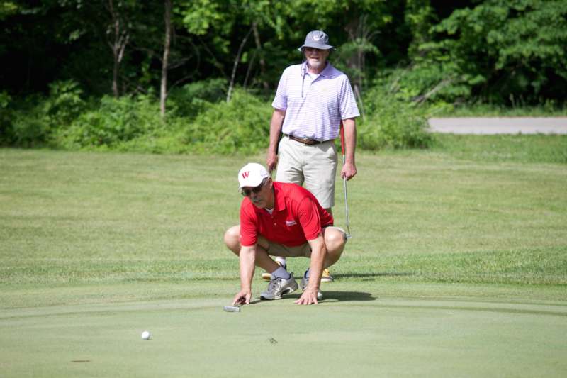a man in a red shirt and white hat kneeling on a green golf course