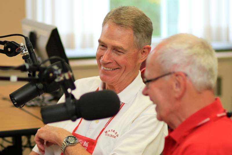 a man in a red shirt smiling next to a microphone