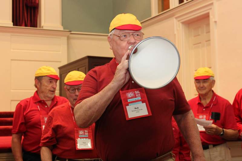 a man wearing a red shirt and yellow hats drinking from a megaphone