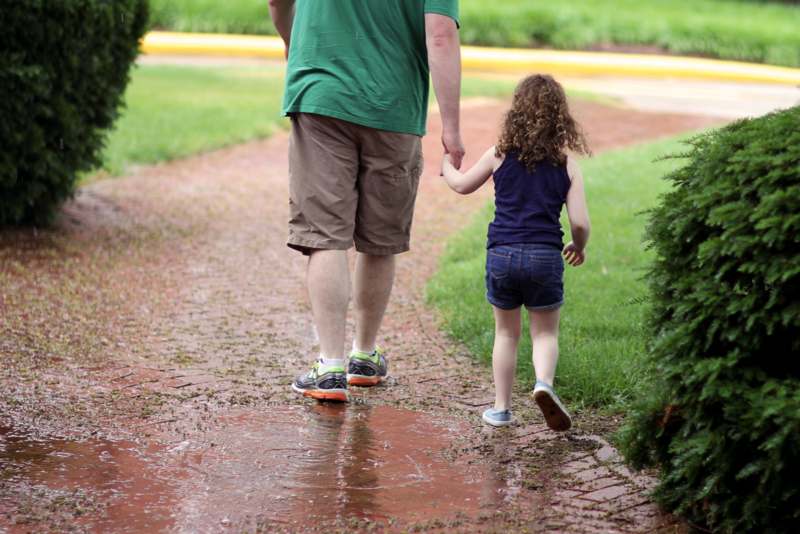 a man and child holding hands walking on a path
