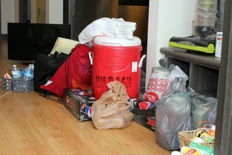 a red cooler with white lid and plastic bags on the floor