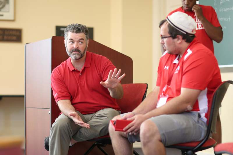 a man in red shirt sitting in a room with other men